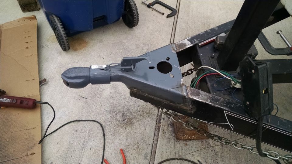 Trailer hitch assembly with a gray coupler, chains, and wiring. A rotary tool is nearby