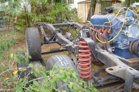 1974 Ford Bronco - The chassis and engine of a vehicle, possibly from the early 1970s, sits outdoors amidst vegetation.