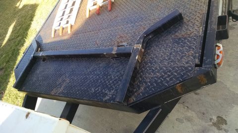 2016 Ford F-250 - Close-up view of a tilt deck with diamond plate texture and metal ramp supports, showing wear and tear.