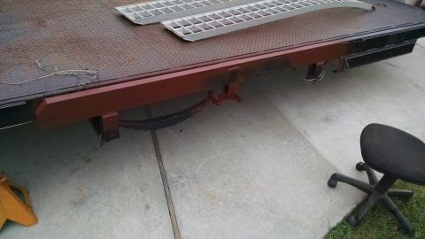 2016 Ford F-250 - Close-up of a rusty tow truck bed, showing its leaf spring suspension and metal ramps.
