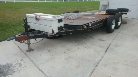 2016 Ford F-250 - A car hauler trailer is parked on a concrete driveway, equipped with a white toolbox mounted on the front tongue.