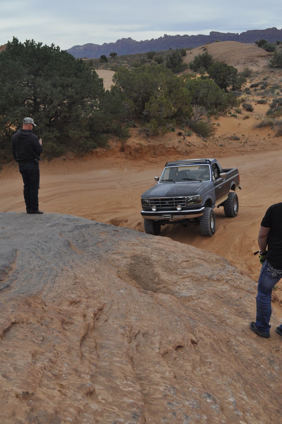 Dark gray Ford F-Series pickup truck with off-road tires driving on a dirt path