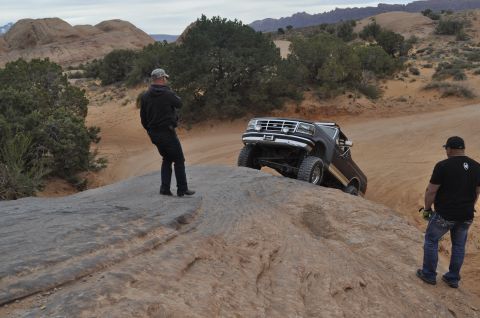 1991 Ford Bronco - A brown Ford Bronco navigates a steep, rocky desert trail with two onlookers.