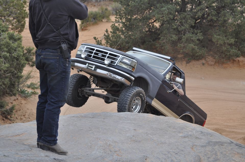 1991 Ford Bronco climbing a large rock with a person standing nearby