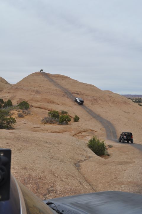 1991 Ford Bronco - Multiple off-road vehicles navigate a challenging rocky incline on a desert trail.
