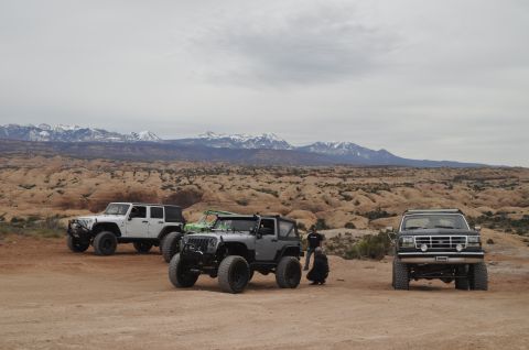 1991 Ford Bronco - A black Ford Bronco is parked in a desert landscape with two Jeeps and mountains in the background.