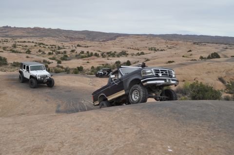 1991 Ford Bronco - Several off-road vehicles navigate a rocky, desert landscape under an overcast sky.