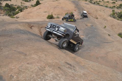 1991 Ford Bronco - Off-road vehicles navigate a challenging rocky trail in a desert landscape.