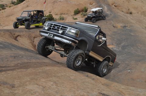 1991 Ford Bronco - A lifted Ford Bronco navigates a steep, rocky trail with other off-road vehicles in the background.