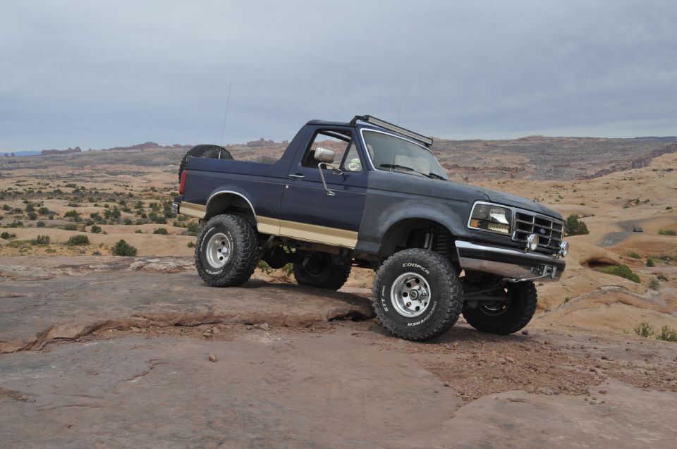 Dark blue Ford Bronco with tan stripe and off-road tires parked on a rocky desert landscape