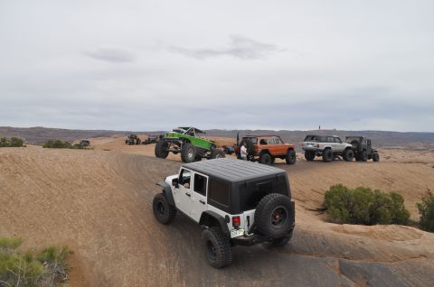 1991 Ford Bronco - A group of modified off-road vehicles traverses a sandy trail in a desert landscape.