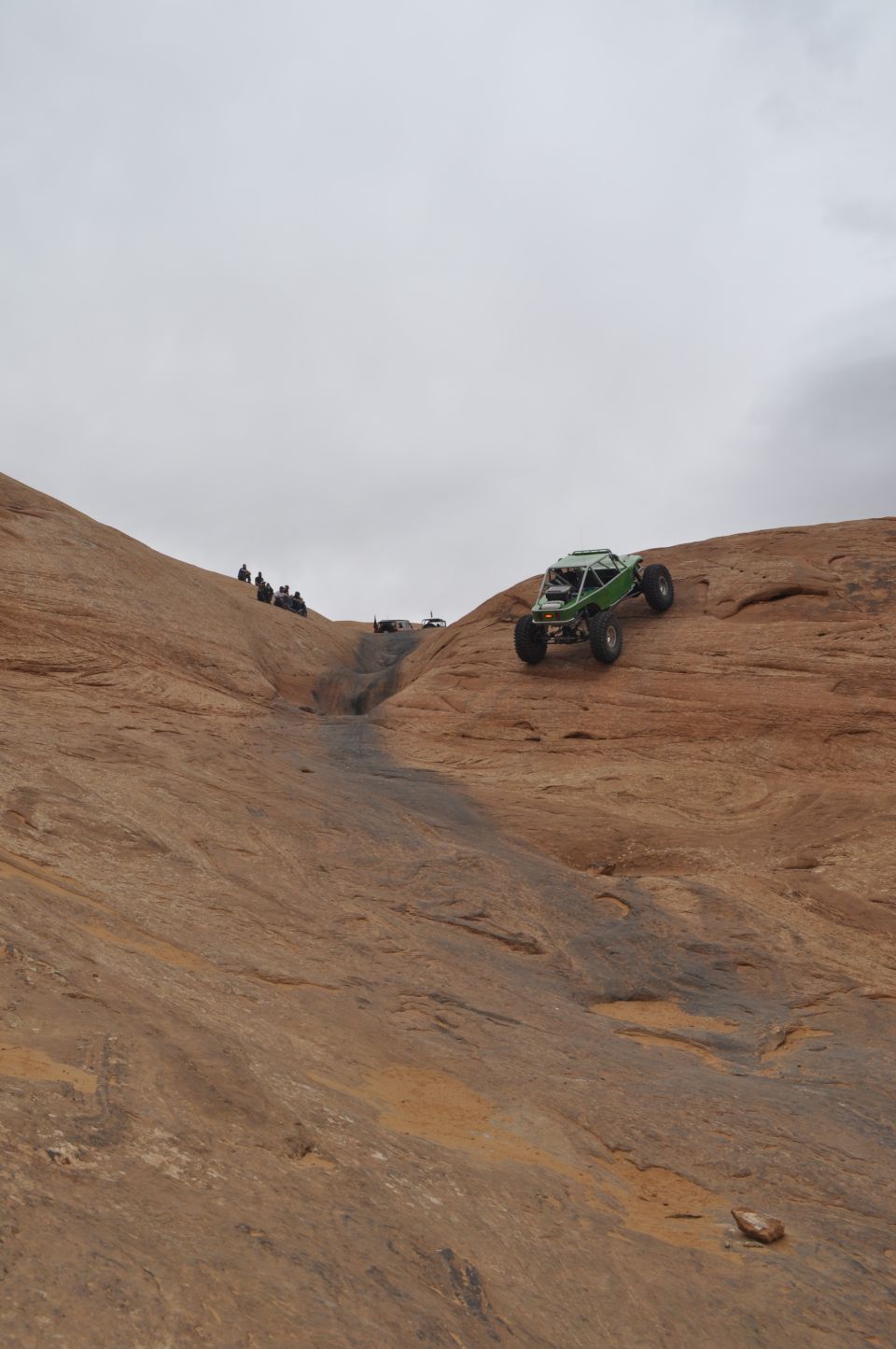 Green off-road buggy climbing a rocky incline with people watching