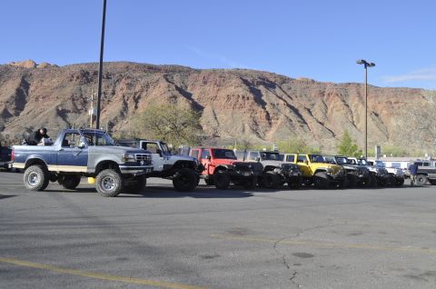 1991 Ford Bronco - A line of off-road vehicles, including a blue and silver Ford Bronco, are parked in a lot with a mountainous backdrop.