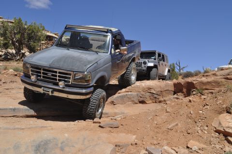 1991 Ford Bronco - A gray Ford F-Series truck leads a convoy of off-road vehicles on a challenging desert trail.