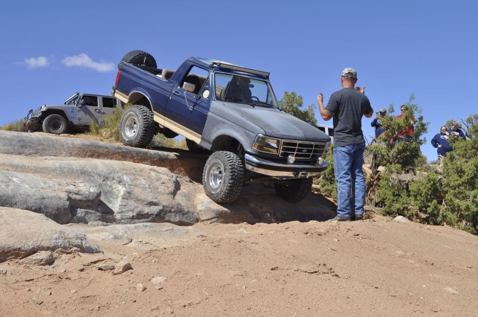Blue and gray Ford Bronco off-roading on rocks, front grille visible