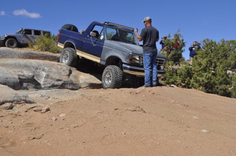 1991 Ford Bronco - A blue and grey Ford Bronco navigates a rocky trail, with a Jeep in the background.