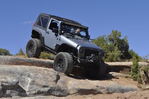 1991 Ford Bronco - Silver Jeep Wrangler navigating a rocky trail under a clear blue sky.