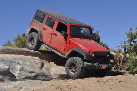 1991 Ford Bronco - A red Jeep Wrangler navigates a challenging rocky trail under a clear blue sky.
