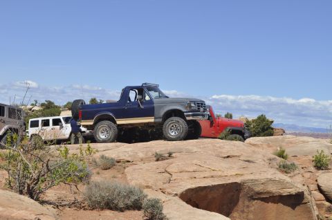 1991 Ford Bronco - A two-tone Ford Bronco is parked on a rocky trail alongside a red Jeep under a clear blue sky.