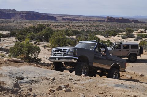 1991 Ford Bronco - Two off-road vehicles, a Ford Bronco and a Jeep Wrangler, traverse a desert landscape.