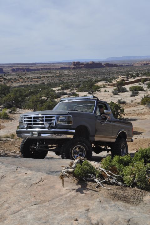 1991 Ford Bronco - A lifted Ford Bronco navigates a rocky, desert landscape under a partly cloudy sky.