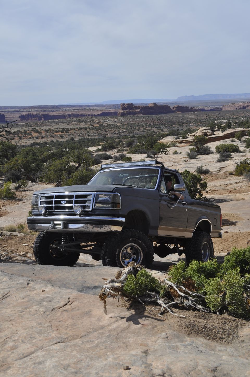 Dark gray lifted Ford Bronco with chrome grille and aftermarket wheels on rocky terrain