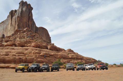 1991 Ford Bronco - Off-road vehicles gathered in a desert landscape with prominent rock formations under a cloudy sky.