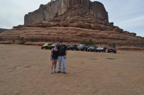 1991 Ford Bronco - A group of SUVs are parked in a desert area with two people in the foreground and a large rock formation behind them.