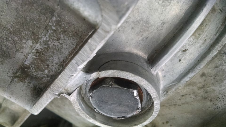 Close-up of a cracked metal housing with a hex bolt. Looks like part of a car's differential