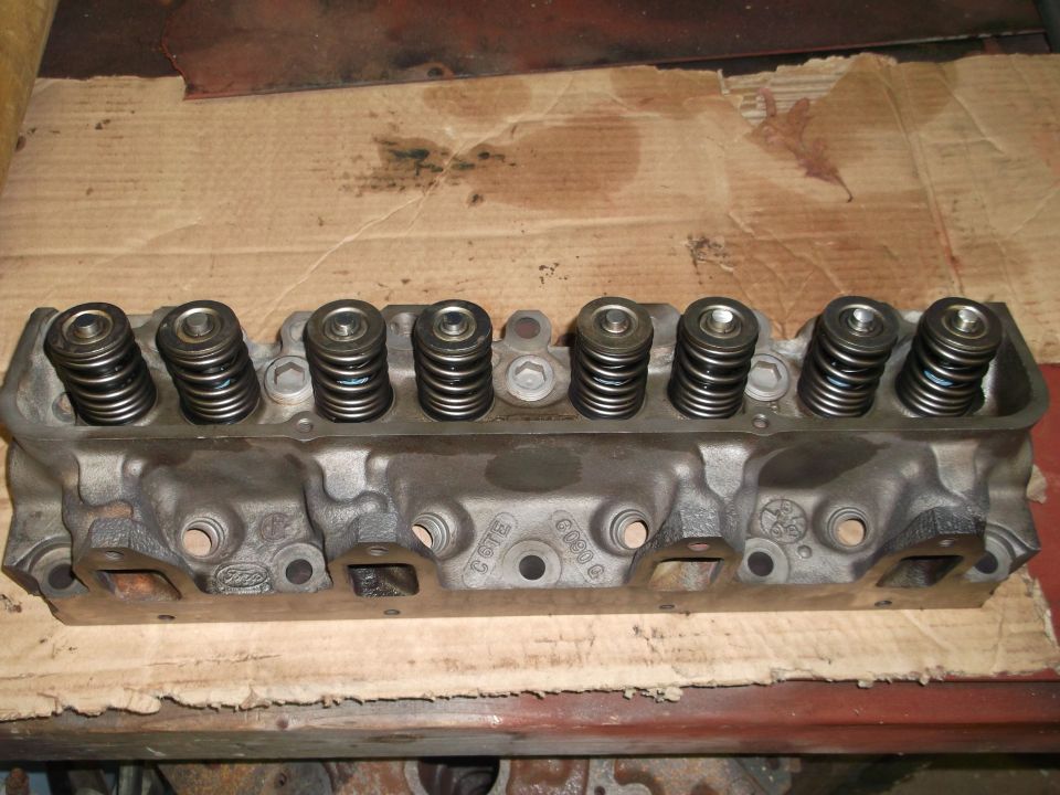 Engine cylinder head with valve springs visible. Ford logo stamped on the side