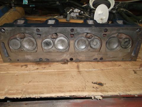 1964 Ford Galaxie - A close-up view of an engine cylinder head, showing its internal components and resting on a wooden surface.