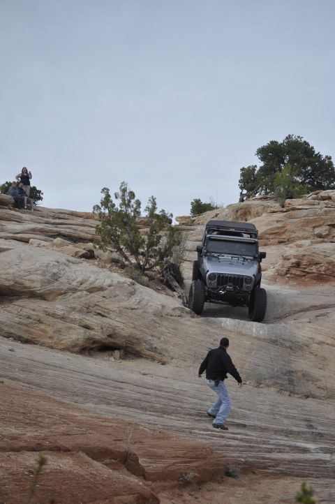 1991 Ford Bronco - A Jeep Wrangler navigates a steep, rocky terrain with onlookers observing from a higher vantage point.