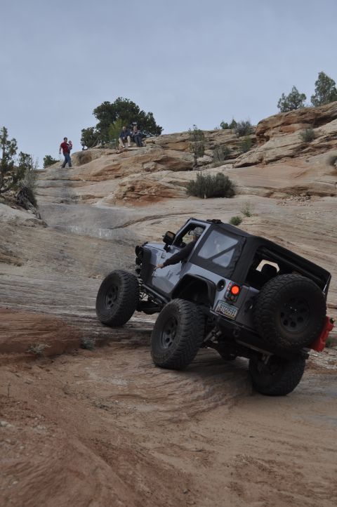 1991 Ford Bronco - A gray Jeep Wrangler navigates a steep, rocky off-road trail with people watching from above.