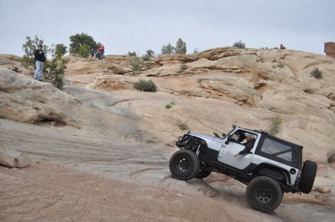 1991 Ford Bronco - A silver Jeep Wrangler navigates a challenging off-road trail in a desert landscape.