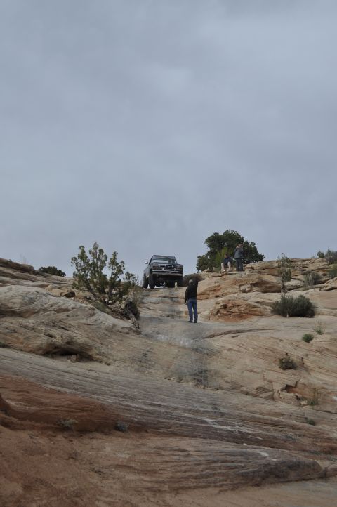 1991 Ford Bronco - A group of people watch as a vintage truck navigates a steep, rocky trail under an overcast sky.