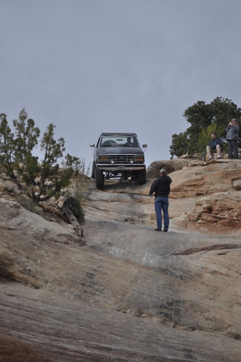 1991 Ford Bronco - A dark gray Ford Bronco navigates a steep, rocky terrain with onlookers observing.