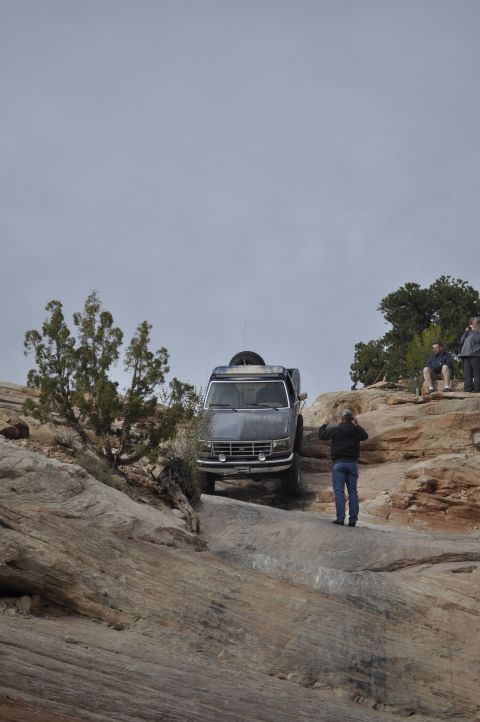1991 Ford Bronco - A gray 1992 Ford Bronco navigates a steep, rocky terrain, with onlookers observing the off-road adventure.