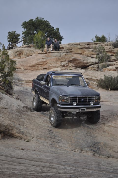1991 Ford Bronco - A lifted Ford Bronco navigates a steep, rocky trail with two onlookers observing from above.