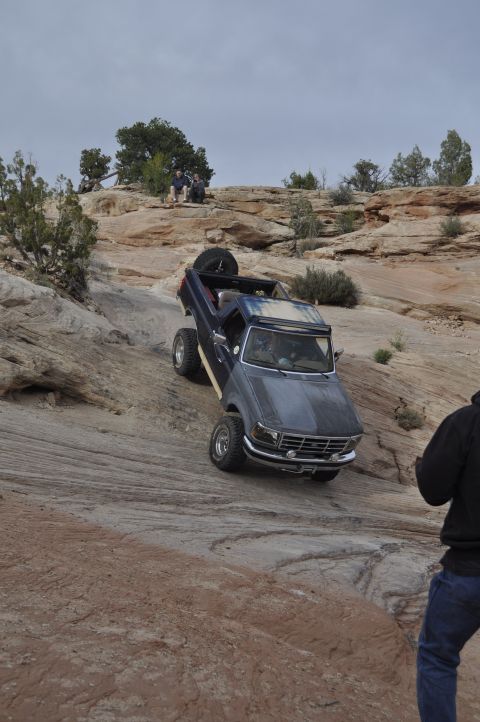 1991 Ford Bronco - A dark blue Ford Bronco navigates a challenging rocky terrain with a spare tire on its back.
