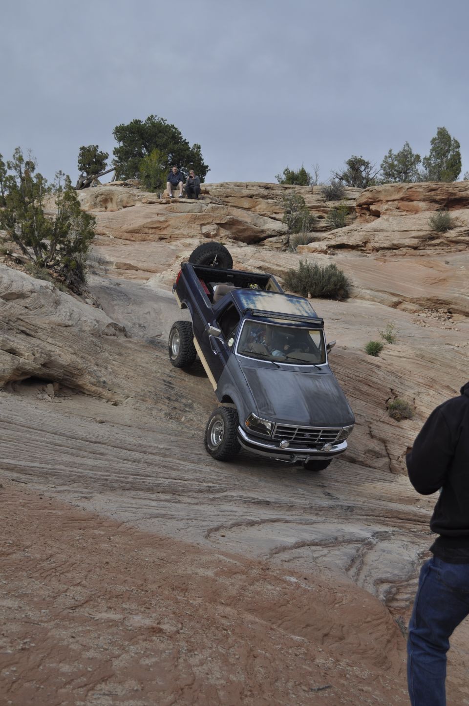Dark blue Ford Bronco climbing a rocky incline, spare tire mounted on rear