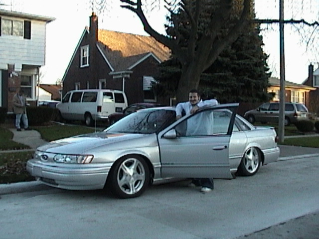guy leaning on silver sedan with doors open, parked on street
