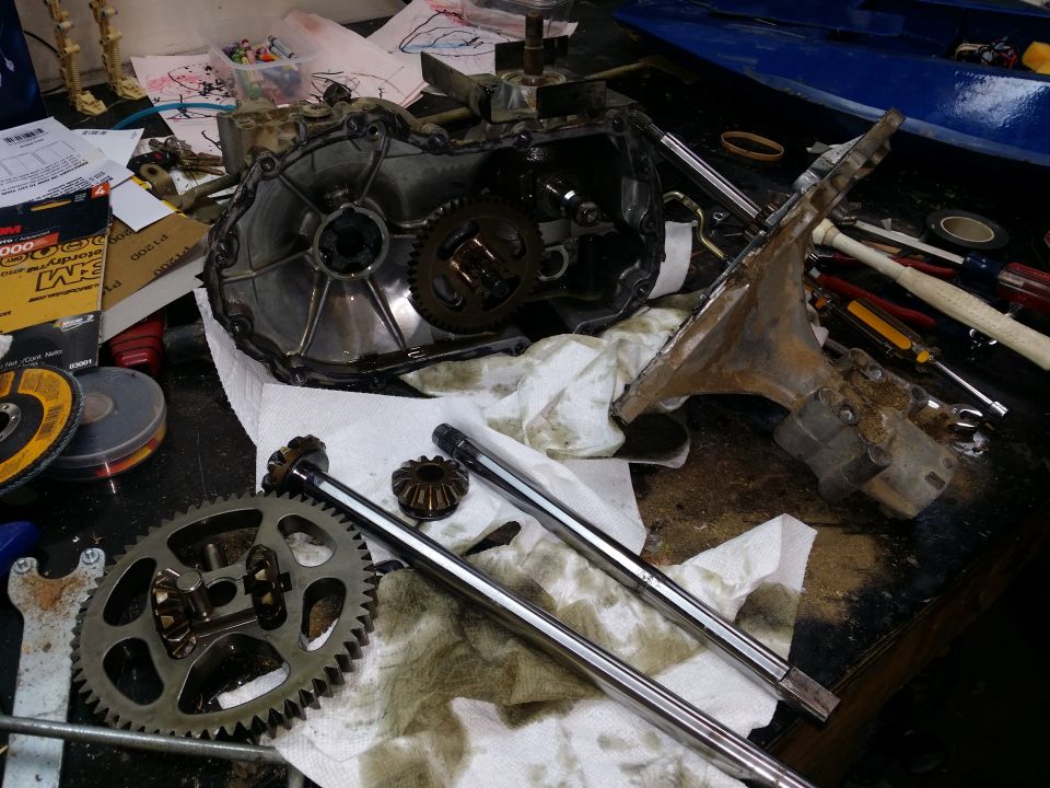 Disassembled transmission or differential with gears and shafts on a workbench, tools and parts scattered around