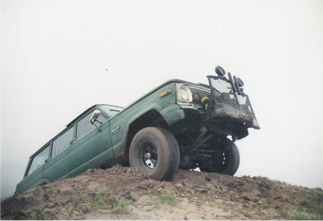 Green vintage 4x4 wagon flexing suspension while climbing a dirt mound off-road