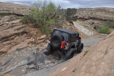 1991 Ford Bronco - A gray Jeep Wrangler navigates a challenging rocky off-road trail in a desert landscape.