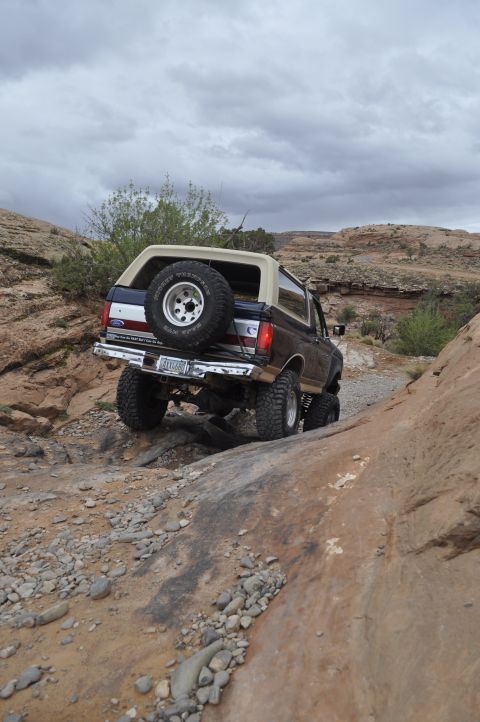 1991 Ford Bronco - A 1991 Ford Bronco navigates a challenging off-road path under a cloudy sky.