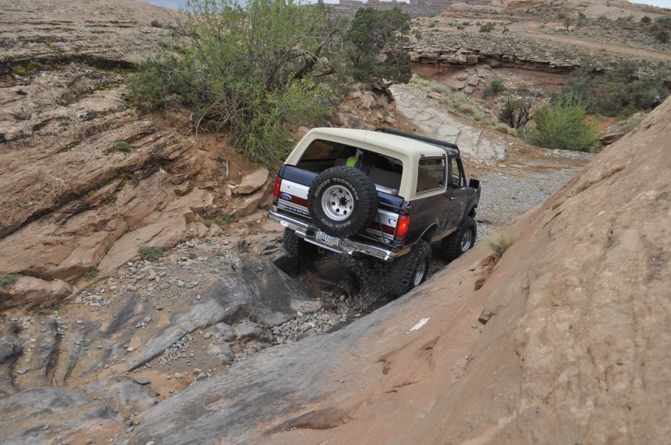 Dark blue 1991 Ford Bronco with a tan top navigates a steep, rocky off-road path