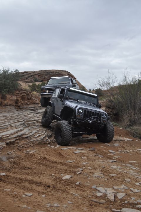 1991 Ford Bronco - Two modified off-road vehicles, a 1991 Ford Bronco and a Jeep Wrangler, navigate a challenging rocky terrain.