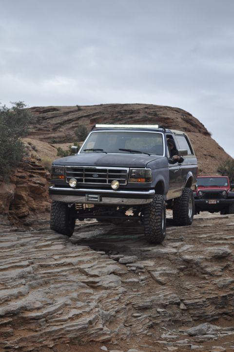 1991 Ford Bronco - A dark blue 1991 Ford Bronco navigates a , rocky terrain, with another vehicle visible behind it.
