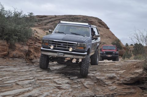 1991 Ford Bronco - Two off-road vehicles, a Ford Bronco and a Jeep Wrangler, navigate a rocky trail under an overcast sky.
