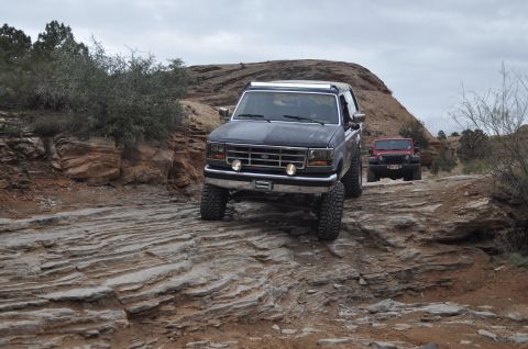 1991 Ford Bronco - Two off-road vehicles navigate a challenging rocky terrain under an overcast sky.